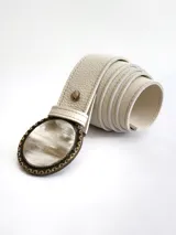 Cinto de cuero color crudo con forro de cuero y sistema de broche suizo intercambiable. Presenta una hebilla circular de guampa con borde metálico labrado en tono bronce.