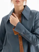 Camisa de cuero ovino color azul, de silueta estructurada, cuello camisero y cierre frontal con broches a presión.
