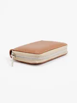 Billetera compacta de cuero plateado, con cierre perimetral y logo grabado en el frente.