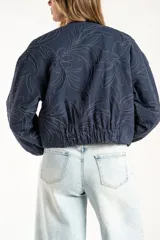 Campera tipo bomber color azul, con cierre frontal y diseño de bordado floral en toda la prenda. Presenta puños y ruedo con elástico, y un corte holgado.