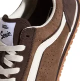 Championes Vans de perfil bajo confeccionados en gamuza color marrón con detalles perforados en los laterales. Presentan la icónica banda lateral en color blanco, cordones blancos y suela de goma con patrón waffle.