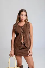 Chaleco de denim celeste sin mangas, confeccionado en algodón. Presenta un cierre frontal con botones forrados en la misma tela y un diseño de bajo redondeado con una abertura central.