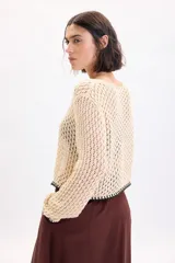 Cardigan de punto fantasía color crudo, con mangas largas y cierre delantero con tiras para atar. Presenta detalles de terminación en color negro en el ruedo y los puños.