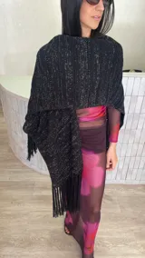 Ruana tejida en color negro con sutiles hilos brillantes, presenta un diseño de textura acanalada con líneas horizontales caladas y terminación en flecos en los extremos.