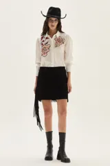 Falda corta de cuero color marrón, con diseño de flecos largos desmontables que cubren toda la prenda. Presenta un estilo western con cierre en la cintura.