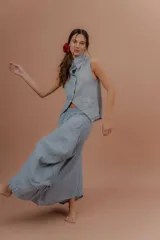 Pollera larga de lino color gris topo, de diseño amplio con volumen, movimiento y bolsillos delanteros. Cuenta con elástico en la cintura y detalles de pinzas y sobretelas en los laterales.