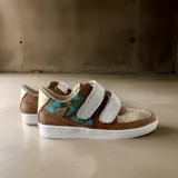 Sneakers urbanos de cuero vacuno en combinación de colores marrón terracota, blanco y dorado, con tiras de velcro y detalles pintados a mano en tono turquesa.