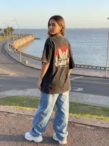 Remera negra con efecto lavado, corte oversize y estampado de palomas y texto en rojo.