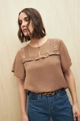 Blusa color marrón con textura sutil, detalle de encaje sobre el canesú y volados. Tiene corte fluido y mangas amplias.