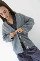 Cárdigan gris de tejido de punto con cuello en V, cierre frontal con botones blancos y mangas largas con puños abotonados.