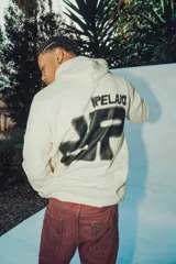 Hoodie color crema de corte oversize con capucha y diseño gráfico en la espalda.