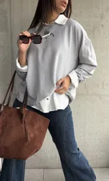 Sweater de punto color gris, de corte holgado y diseño de manga larga con costuras visibles en los hombros. Presenta cuello redondo y puños acanalados.