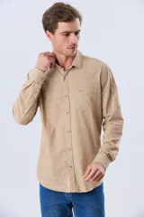 Camisa de lino de manga larga en color beige, con cuello camisero, cierre frontal de botones y un bolsillo ojal en el pecho.