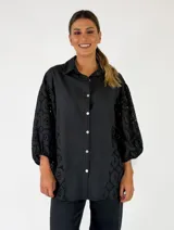 Camisa de manga larga color negro, con cuello clásico, cierre frontal con botones y laterales y mangas confeccionados en tejido broderie con diseño geométrico calado.