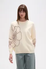 Sweater de tejido de punto color crema, con diseño holgado, cuello redondo a la base y mangas largas. Presenta apliques bordados en relieve con forma de flores en tonos rosados en el frente y las mangas.