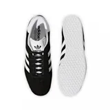 Championes adidas modelo Gazelle, confeccionados en gamuza negra con las icónicas tres tiras laterales y refuerzo en el talón en color blanco. Presenta suela de goma blanca y el nombre del modelo en letras doradas en el lateral.