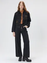 Campera de denim oscuro con corte crop, cierre frontal con botones metálicos, bolsillos delanteros con detalles bordados y apliques metálicos en el pecho.