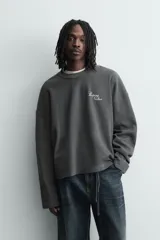 Sudadera de corte relajado confeccionada en tejido de algodón con textura acanalada. Presenta cuello redondo, manga larga y un diseño con efecto lavado. Incluye un texto estampado en contraste en la parte frontal.