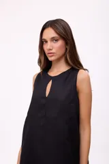 Vestido corto beige de lino, sin mangas, con escote redondo y detalle de abertura en forma de lágrima en el pecho. Presenta diseño holgado y dobladillo asimétrico más largo en la parte trasera con volados.