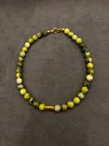 Collar corto de piedras volcánicas marrones y marrones oscuras, con detalle cilíndrico dorado en el centro.