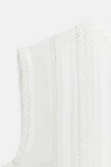 Blusa sin mangas de algodón con cuello redondo, diseño con paneles verticales bordados y detalles de encaje, cierre posterior con abertura y botón.
