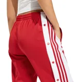 Pantalon deportivo Adidas modelo Adibreak, color rojo con franjas laterales blancas y las icónicas tres tiras en rojo. Presenta botones a presión a lo largo de los laterales y cintura elástica.