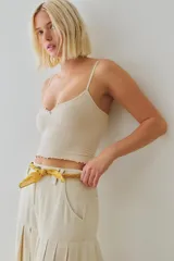 Top corto sin costuras de tejido acanalado y texturado color marfil, con escote redondo amplio, botonadura henley al frente con pequeños botones a presión, tiras finas fijas y terminación con ruedo en lechuga, de calce ajustado.
