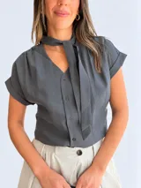 Blusa gris oscuro de rayón y poliéster, con escote en V, cierre frontal de botones, mangas cortas con vuelta y cuello con lazo incorporado para anudar.