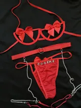 Conjunto de lencería rojo compuesto por soutienne con aros y moños decorativos, bombacha vedetina con letras de strass y tiras regulables, y portaligas con arnés y cadenas de brillantes.