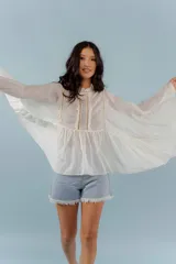 Camisa de algodón con diseño romántico, mangas amplias y detalles de puntillas verticales en el frente. Presenta un corte holgado y fluido.