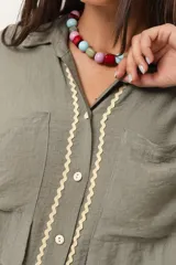 Camisa verde militar de manga larga con silueta oversize, dos bolsillos delanteros y corte levemente más largo en la espalda. Escote en V abotonado con detalle de galón picot a lo largo de la cartera y botones a tono. Isotipo bordado en la parte trasera.