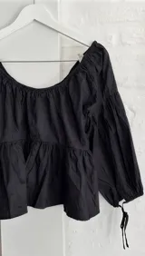 Blusa negra de manga larga abullonada con tiras ajustables en los puños, escote bote elastizado y diseño holgado con corte evase.