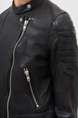 Campera de cuero ovino color negro, con cierre frontal asimétrico, cuello redondo con broche a presión y cierres metálicos en los puños.