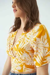 Blusa estampada con diseño de hojas en color amarillo y blanco, con escote en V cruzado, mangas cortas y elástico en la cintura.