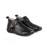 Botita baja Marcel confeccionada en cuero vacuno color marrón, con interior de corderito ultrasuave. Presenta costuras pespunteadas decorativas, tira lateral con hebilla metálica dorada y detalles de elástico negro. Suela plana de goma negra.