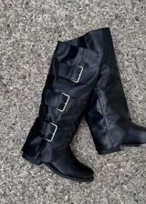 Botas de caña alta confeccionadas en ecocuero negro, con diseño de tres hebillas metálicas laterales y suela plana.
