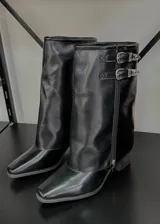 Botas de caña media negras, con punta fina, taco bajo y cierre lateral con cremallera. Presentan dos correas con hebillas metálicas decorativas en la parte superior.