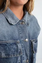 Campera de denim azul con calce boxy, cuello clásico, cierre con botones metálicos, mangas largas con puños abotonados, dos bolsillos frontales con solapa y parche con logo en el frente.