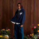 Campera tipo canguro con cierre frontal, color azul marino, de corte holgado y mangas abullonadas con puños ajustados. Presenta un bordado blanco con un monograma estilizado en el pecho.