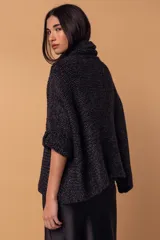 Sweater tipo poncho de tejido de punto grueso en color negro, con cuello alto tipo polera y mangas tres cuartos con puños vueltos.