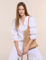 Blusa blanca de calce suelto y caída ligera, con escote en V y cuello Mao pequeño. Presenta mangas tres cuartos abullonadas con elástico en los puños y detalles de calado o puntilla encastrada. Espalda lisa con canesú y leve frunce.