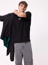 Campera reversible con cuello alto y cierre frontal. Un lado presenta tejido de polar con estampado geométrico en tonos verdes y bolsillo con cierre en el pecho, mientras que el otro lado es de nylon. Cuenta con puños elásticos y bolsillos laterales.
