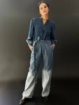 Mono largo de jean azul con lavado artesanal, escote en V regulable con cierre invisible, mangas largas abullonadas y lazo en la cintura.