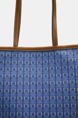 Bolso tipo tote de hombro con cuerpo estampado en tonos azules con patrón geométrico. Cuenta con detalles en tono tostado en las asas dobles, bordes y costuras en contraste. Cierre mediante botón imantado y compartimento interior.
