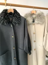 Sacón de lana merino color beige, con cuello de piel sintética, cierre frontal con botones, mangas abullonadas con puños elásticos y bolsillos frontales.