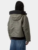 Chaqueta corta tipo bomber con capucha, color verde militar, con cierre frontal de cremallera y botones, bolsillos laterales con solapa y bolsillo utilitario en la manga.