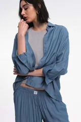 Camisa color marrón de corte oversized, con abotonadura frontal y en las mangas. Presenta un corte vertical en la espalda con lazos decorativos.