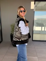 Chaleco reversible con un lado de piel sintética gris y el otro lado de tela bordada con diseño floral y espiral en tonos blanco y negro. Presenta un diseño sin mangas y corte recto.