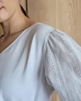 Remera blanca con cuello en V, cuerpo de algodón y mangas abullonadas de encaje bordado con puños elásticos.