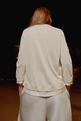 Chaqueta efecto doble de punto color beige con cuello redondo, manga por debajo del codo y cierre frontal con botones. Detalle de cuello y bajo de camisa interior asomados.